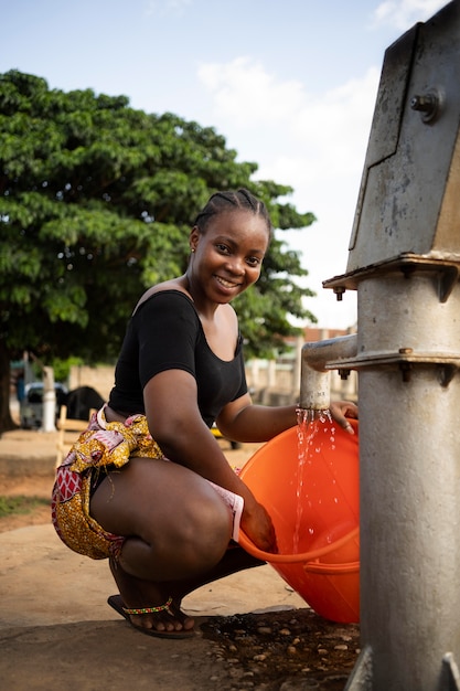Beautiful african woman putting some water in a bucket