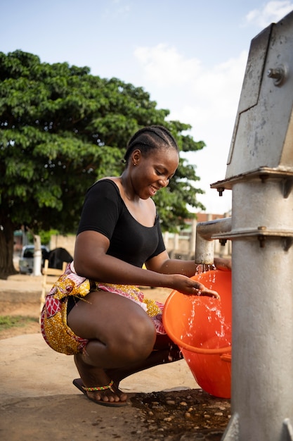 Foto gratuita bella donna africana che mette dell'acqua in un secchio