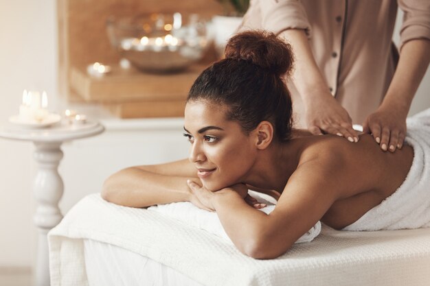 Beautiful african woman smiling enjoying massage in spa resort.