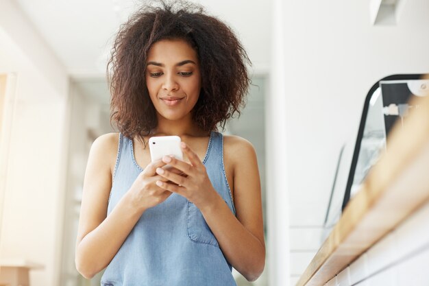 カフェに座っている携帯電話の画面を見て笑っている美しいアフリカ人女性。