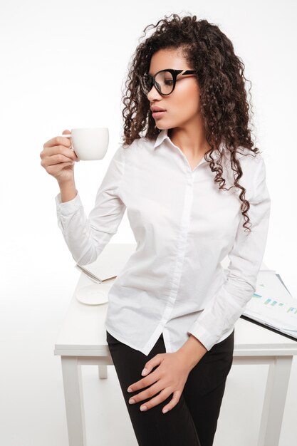 Beautiful african young businesswoman in glasses standing and drinking coffee