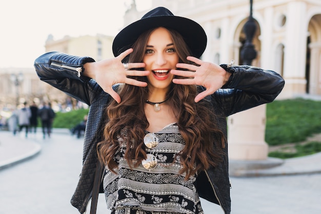 Beautiful amazing brunette woman with long wavy hairstyle in spring or fall stylish urban outfit walking on the street. Red lips, slim body. Street fashion concept.