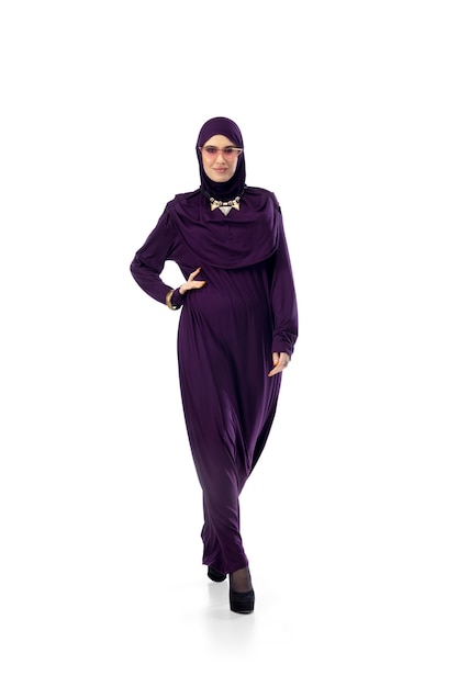 스튜디오 벽에 격리된 세련된 히잡을 입고 포즈를 취한 아름다운 아랍 여성