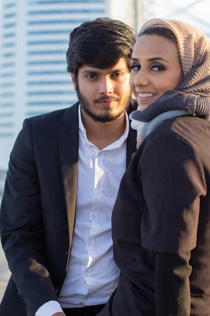 beautiful arabic couple spending time together. woman with covered head and bright make-up and man in suit sitting looking at camera. love, affection concept