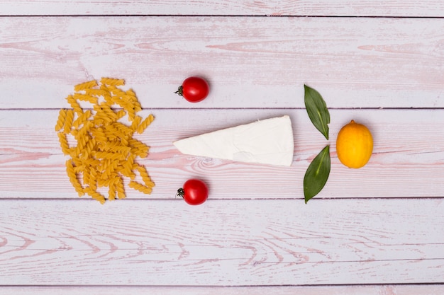 Бесплатное фото Красивое расположение сырой пасты фузилли; томаты; сыр; лавровый лист и лимон на деревянном фоне