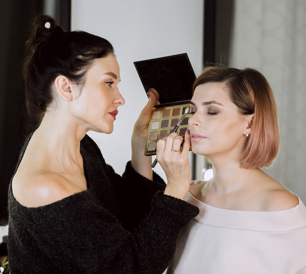 Beautiful artist applying make-up on model
