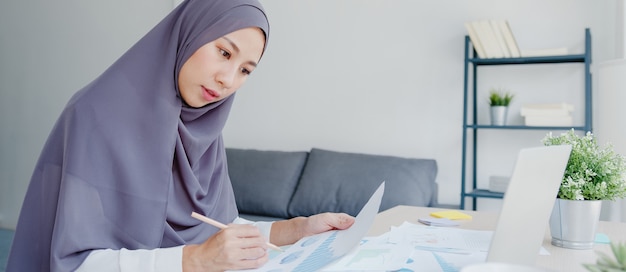 Beautiful Asia muslim lady in headscarf casual wear using laptop in living room at house.