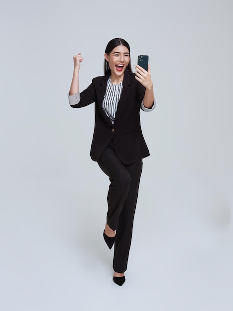 Beautiful Asian businesswoman using mobile phone and happy celebration on white studio background