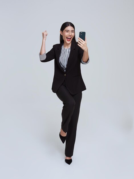 흰색 스튜디오 배경에서 휴대폰과 행복한 축하를 사용하는 아름다운 아시아 여성