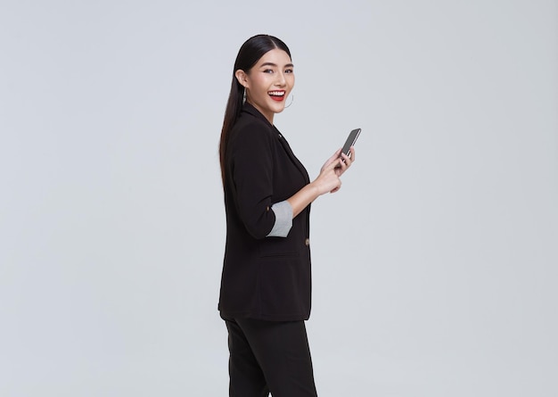 흰색 스튜디오 배경에서 휴대폰과 행복한 축하를 사용하는 아름다운 아시아 여성