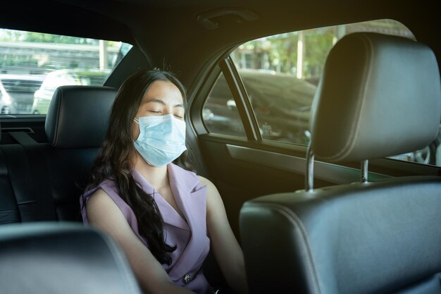 아름다운 아시아 여성 사업가는 위생 보호용 안면 마스크를 쓰고 택시 초상화에서 뒷자리에 앉고, 행복한 아시아 여성 승객은 covid-19 전염병 동안 택시를 이용하여 여행합니다.