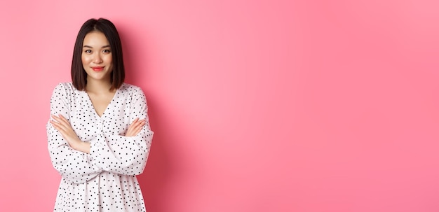 Free photo beautiful asian female model standing in dress cross arms on chest and smiling at camera standing ov