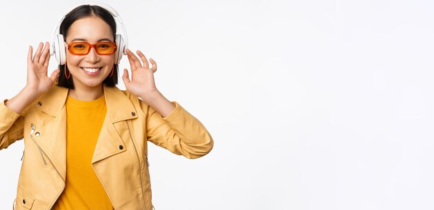 Beautiful asian girl laughing happy listening music in headphones standing over white background Copy space