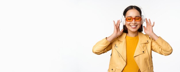 Beautiful asian girl laughing happy listening music in headphones standing over white background