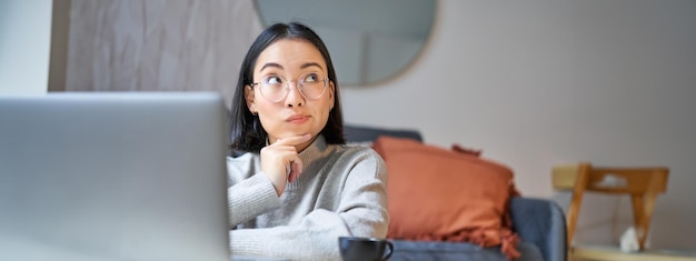 무료 사진 아름다운 아시아 소녀는 원격에 있는 거실에 앉아 노트북을 가지고 집에서 공부합니다.