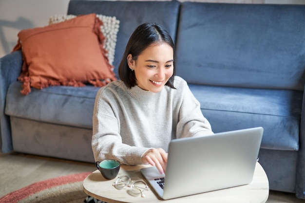 Free photo beautiful asian girl works from home studying with laptop sitting in living room being on remote fre