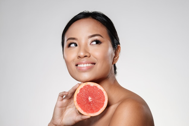 beautiful asian lady looking aside and holding grapefruit slice near face