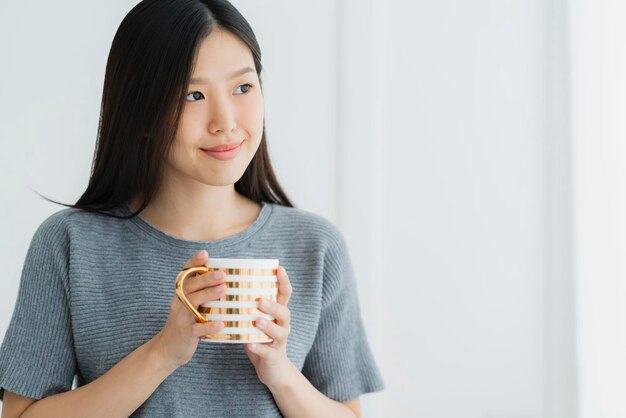 Beautiful asian teen white Tank top happiness smile enjoy freshness morning with hot drink near window with sun light