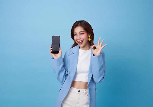 Красивая азиатская подростка держит макет смартфона с пустым экраном и показывает знак ok