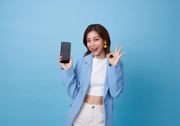 Beautiful Asian teen woman holding smartphone mockup of blank screen and shows ok sign