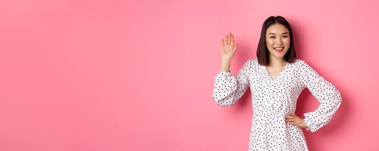 무료 Photo 드레스를 입은 아름다운 아시아 여성이 손을 흔들며 인사하고 친근한 미소를 지었다고 말했습니다.