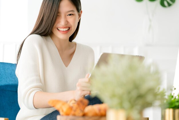 무료 사진 아름다운 아시아 여성은 주말에 스마트폰을 들고 행복과 즐거운 거실 인테리어 배경으로 소셜 미디어를 소통하는 것을 즐깁니다.