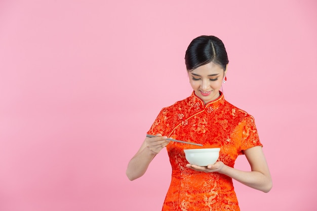 Beautiful Asian woman happy smile and eating in chinese new year on pink background.