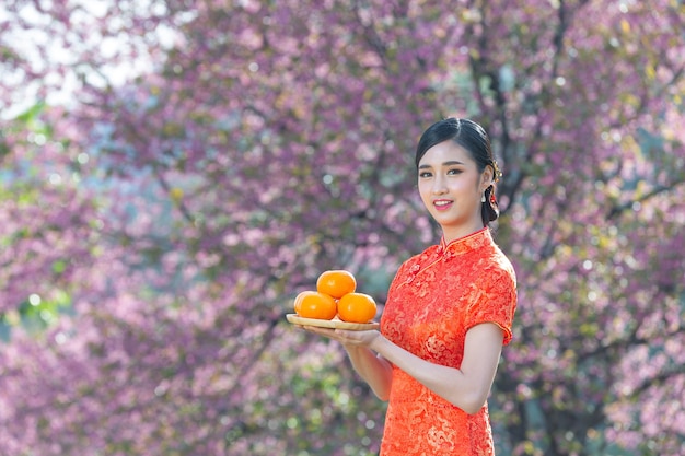 Sorriso felice della bella donna asiatica e che tiene le arance fresche nel nuovo anno cinese su fondo rosa.