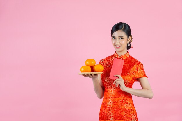 Улыбка красивой азиатской женщины счастливая и держа свежие апельсины в китайском Новом году на розовом фоне.
