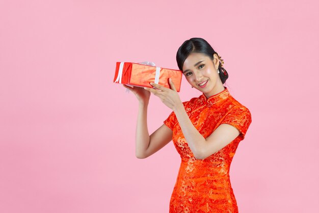 Улыбка красивой азиатской женщины счастливая и держа подарочную коробку в китайском Новом году на розовом фоне.