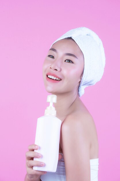 ピンクの背景に製品の瓶を持って美しいアジアの女性。