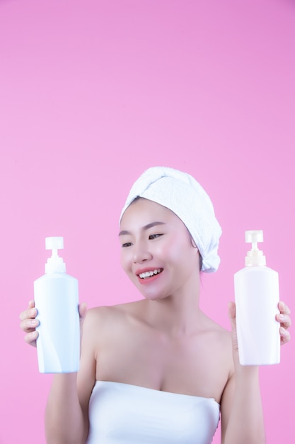 Free photo beautiful asian woman holding a bottle of product on a pink background.