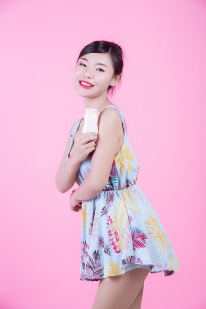 Beautiful Asian woman holding a bottle of product on a pink background.