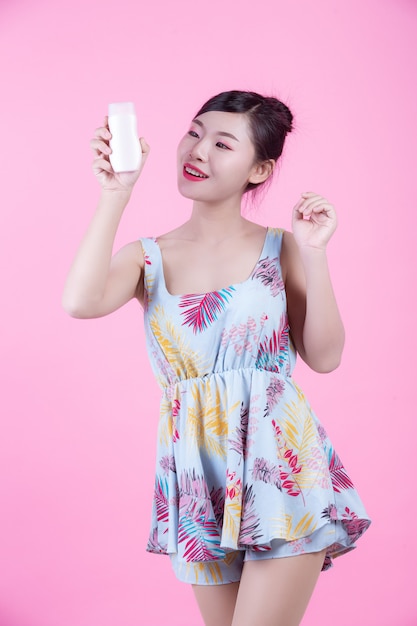 Beautiful Asian woman holding a bottle of product on a pink background.