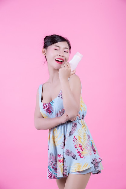Красивая азиатская женщина держа бутылку продукта на розовой предпосылке.