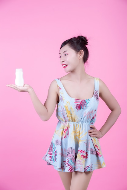 Beautiful Asian woman holding a bottle of product on a pink background.