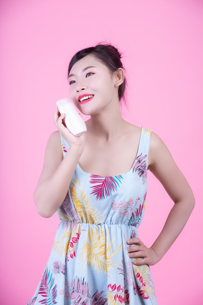 ピンクの背景に製品の瓶を持って美しいアジアの女性。