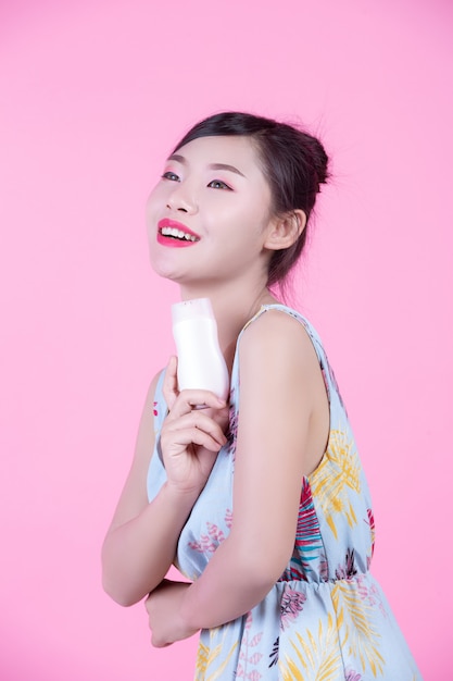 Beautiful asian woman holding a bottle of product on a pink background.