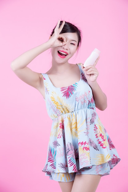 Beautiful Asian woman holding a bottle of product on a pink background.