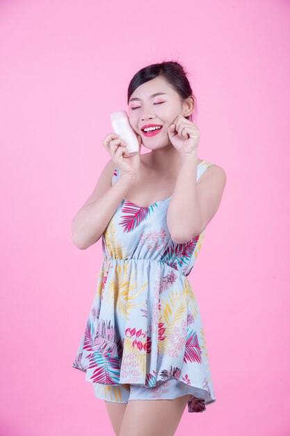 Beautiful Asian woman holding a bottle of product on a pink background.