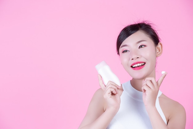 Beautiful Asian woman holding a bottle of product on a pink background.