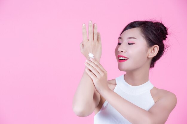 Beautiful Asian woman holding a bottle of product on a pink background.