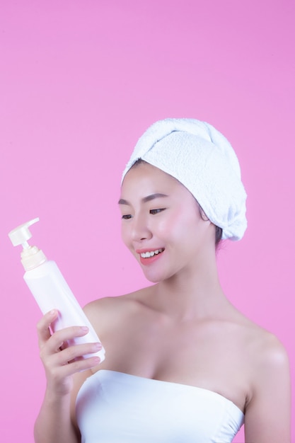 Beautiful Asian woman holding a bottle of product on a pink background.