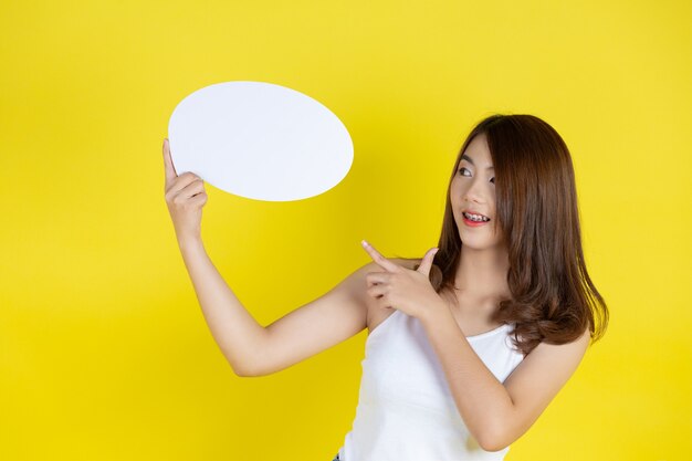 Beautiful asian woman holding and looking up to speech bubble with empty space for text on yellow wall
