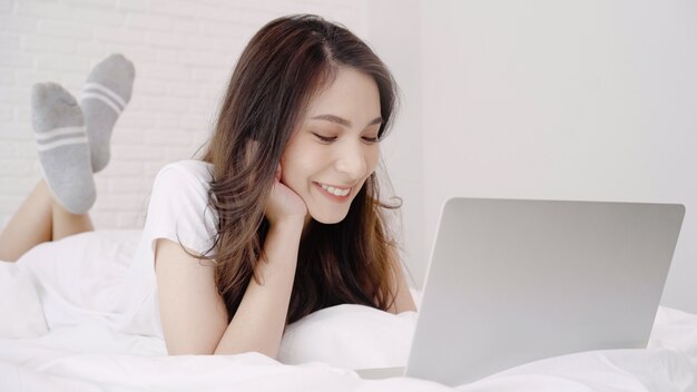 그녀의 침실에서 침대에 누워있는 동안 컴퓨터 또는 노트북을 재생하는 아름 다운 아시아 여자.