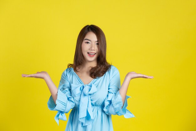 Beautiful asian woman pointing hand to empty space aside on yellow wall