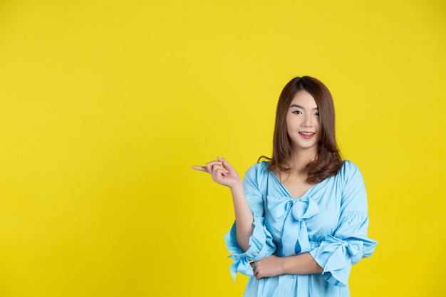 Beautiful asian woman pointing hand to empty space aside on yellow wall