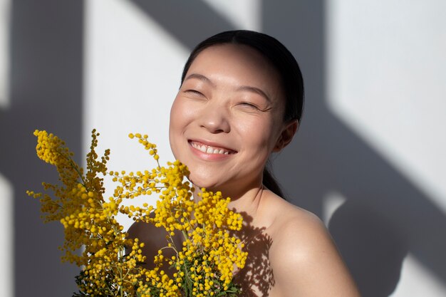完璧な肌で黄色い花を持ってポーズをとる美しいアジアの女性