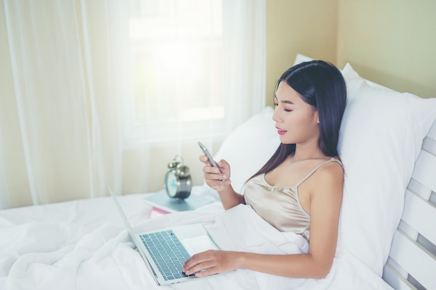 A beautiful Asian woman relaxes and works with a laptop computer, reading at home.