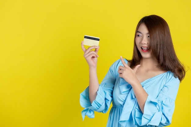 黄色の壁にクレジットカードを示す美しいアジアの女性
